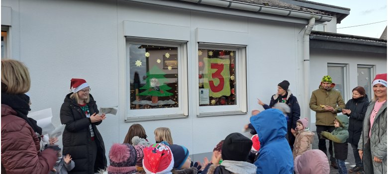 Mehrere Erwachsene und Kinder stehen vor einem geschmückten Fenster