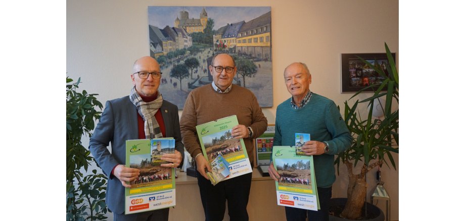 Joachim Rogalski (Mitte) und Walter Reis (rechts) übergeben den Wanderplan 2025 an Oberbürgermeister Dirk Meid