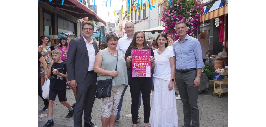 6 Personen stehen in einer Einkaufsstraße - eine hält das Plakat zur Veranstaltung in den Händen