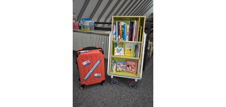 Ein Bücherregal auf Rollen mit Kinderbüchern und ein Medienkoffer