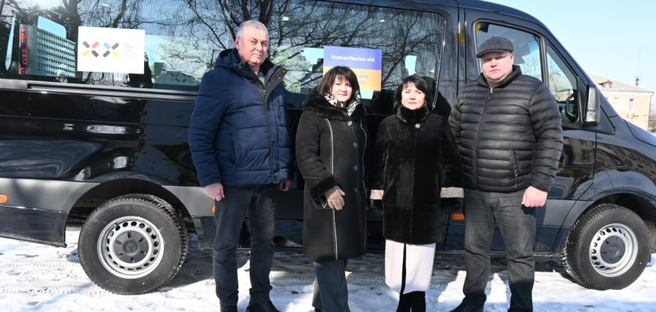 4 Personen stehen vor einem schwarzen Bus